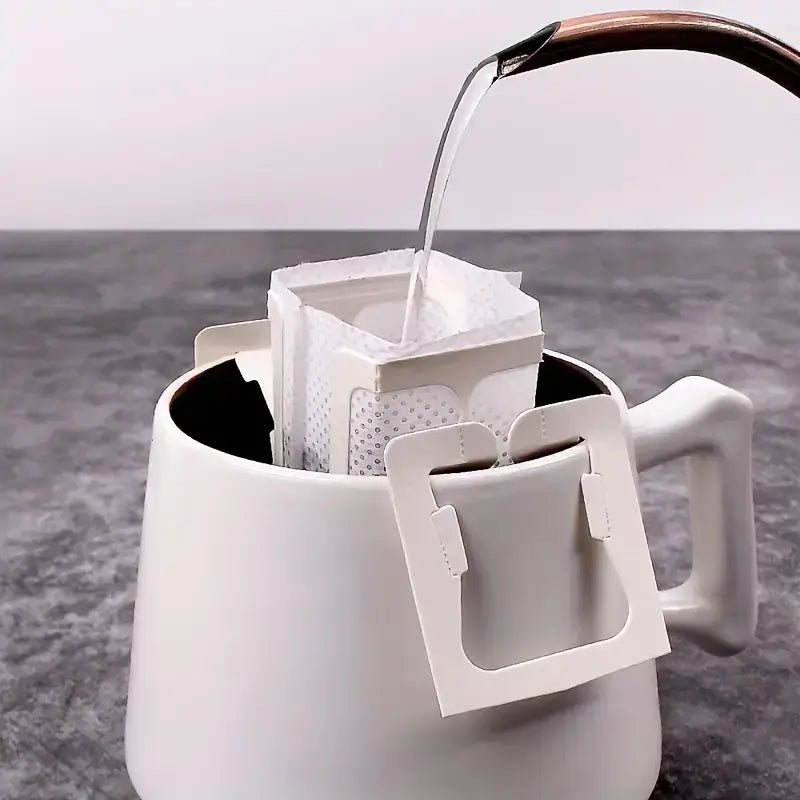 Coffee drip bags in use over a mug with hot water being poured in