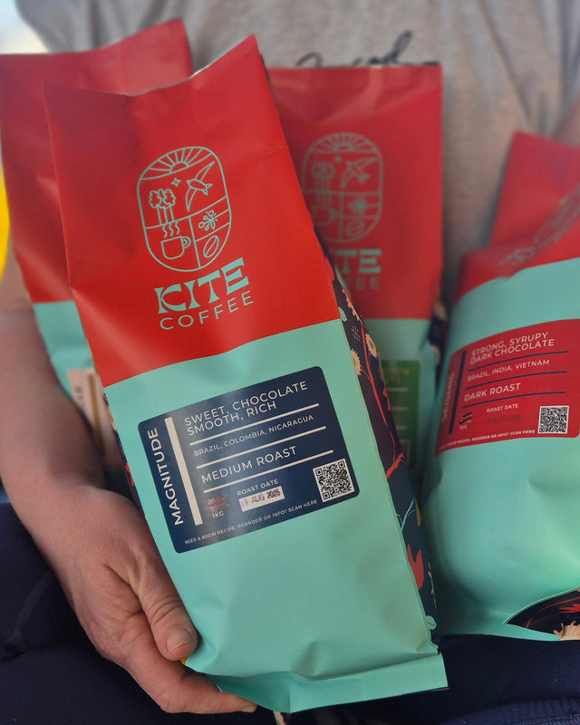 A person holding 4 bags of Kite Coffee 1kg beans